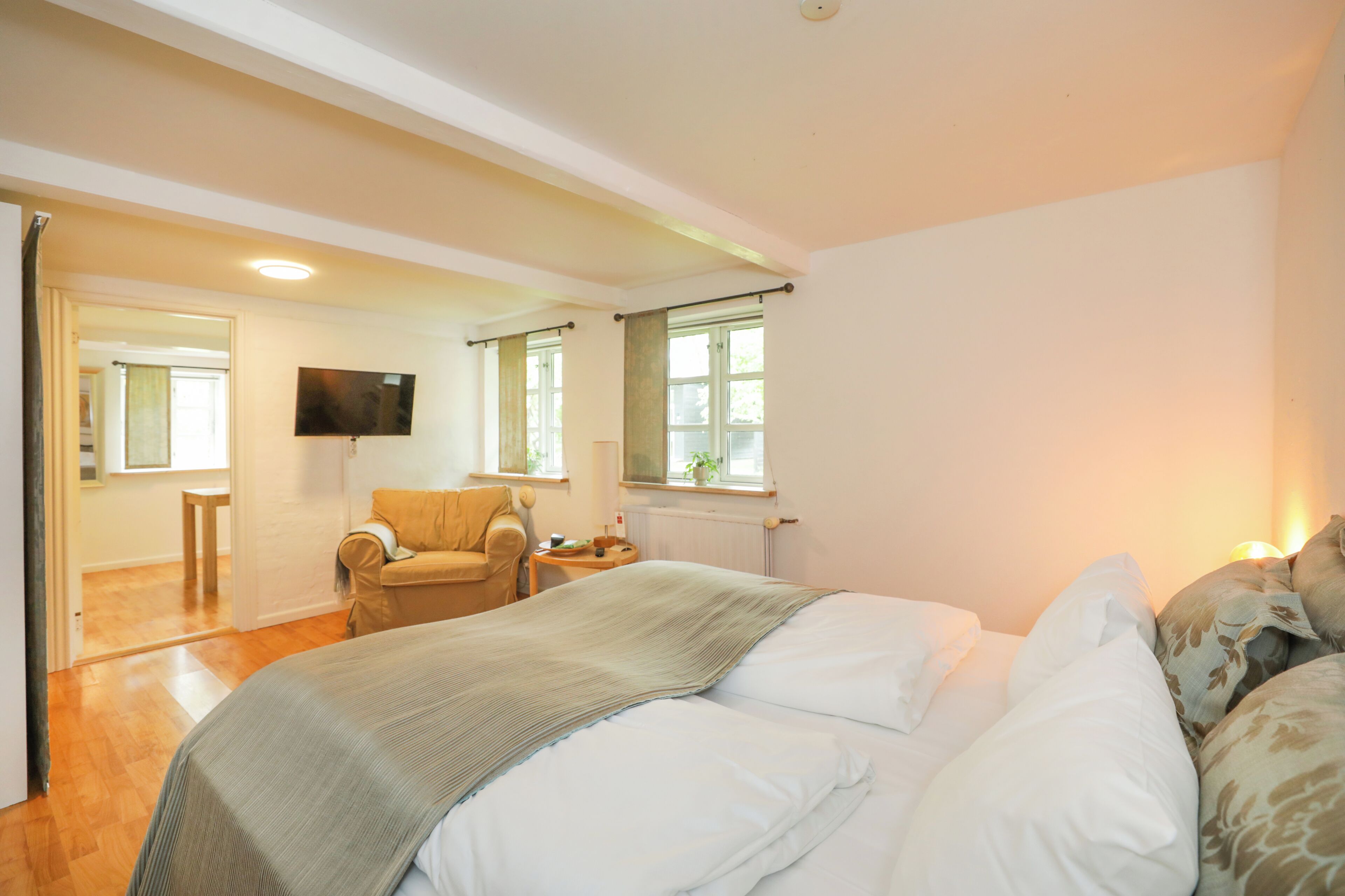 Un dormitorio con cama, una silla, un televisor y una ventana.