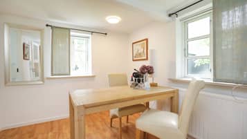 A dining area with a wooden table, chairs, a vase with flowers, and a painting on the wall.