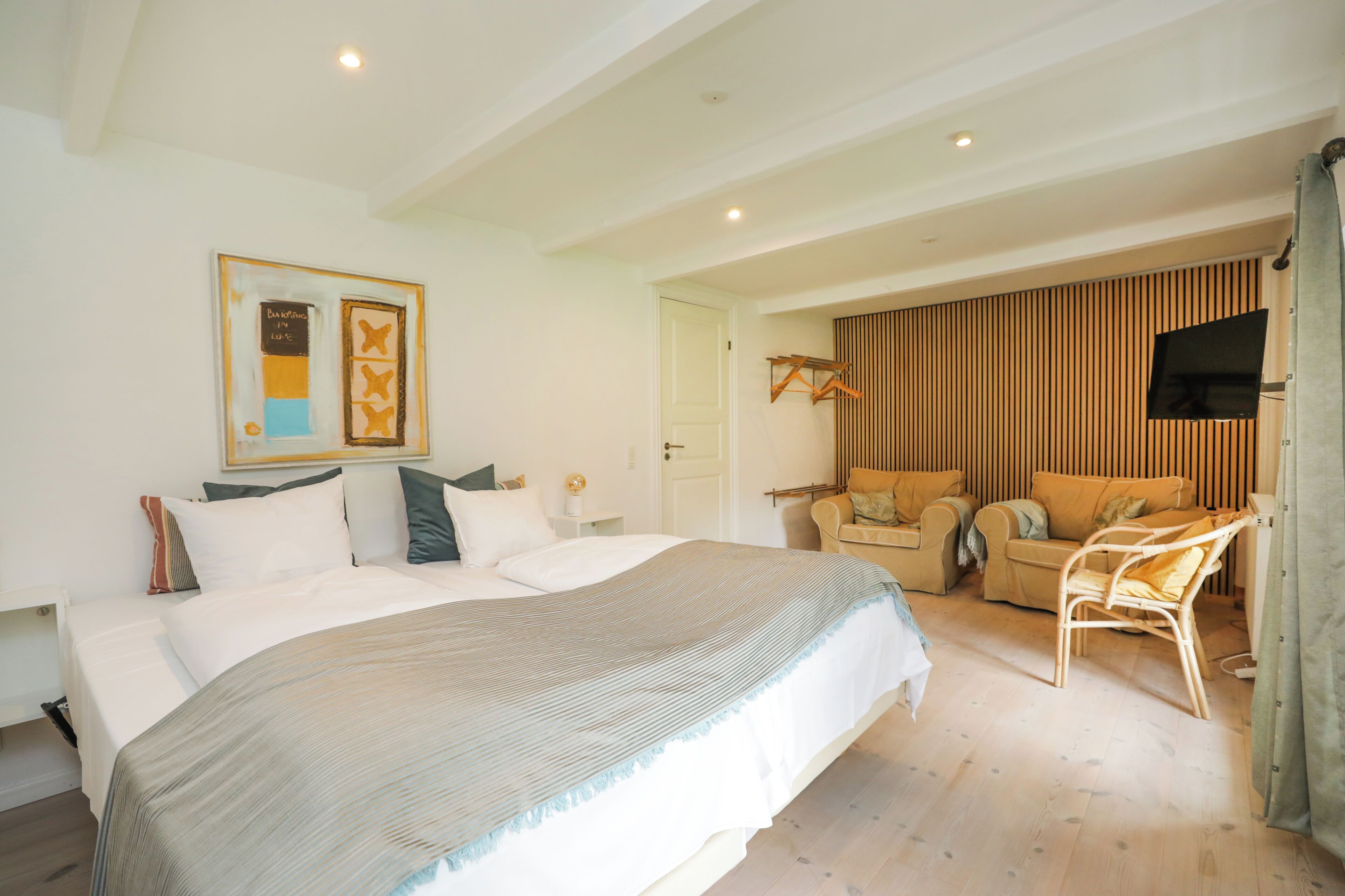 A hotel room with a large bed, a sofa, a chair, a TV, and a wooden panel wall.