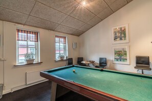 A pool table with a ball, two windows with plaid curtains, and two framed pictures on the wall.