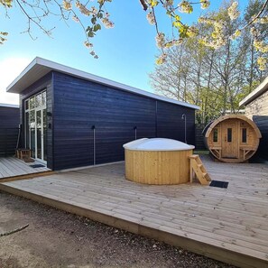 A modern wooden cabin with a hot tub, a sauna, and a deck.
