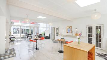 A bright, spacious room with a high ceiling, large windows, and a central wooden table.