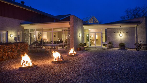 A building with a name sign 'Vilcon' and a gravel driveway with three lit fires. - Vilcon Hotel & Konferencegaard (Slagelse)