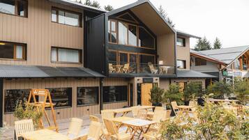 A modern building with a wooden facade, outdoor seating area with wooden tables and chairs, and a sign indicating a restaurant.