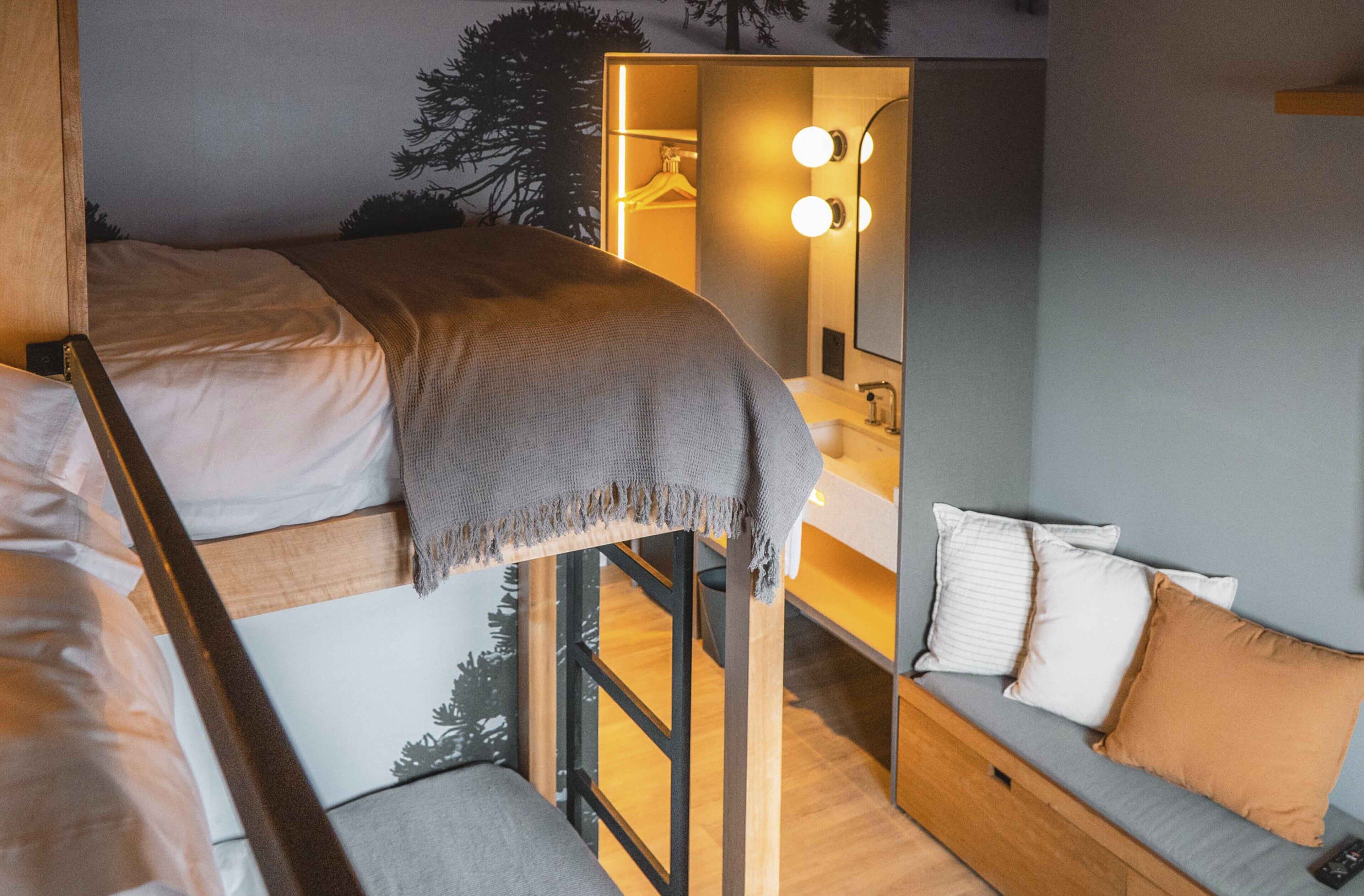 Ein Stockbett mit Decke, eine Couch mit Kissen, ein Spiegel mit Beleuchtung und ein Holzboden.