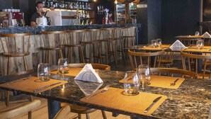 Un restaurante con asientos de bar, sillas de madera y mesas dispuestas con cubiertos y vasos.