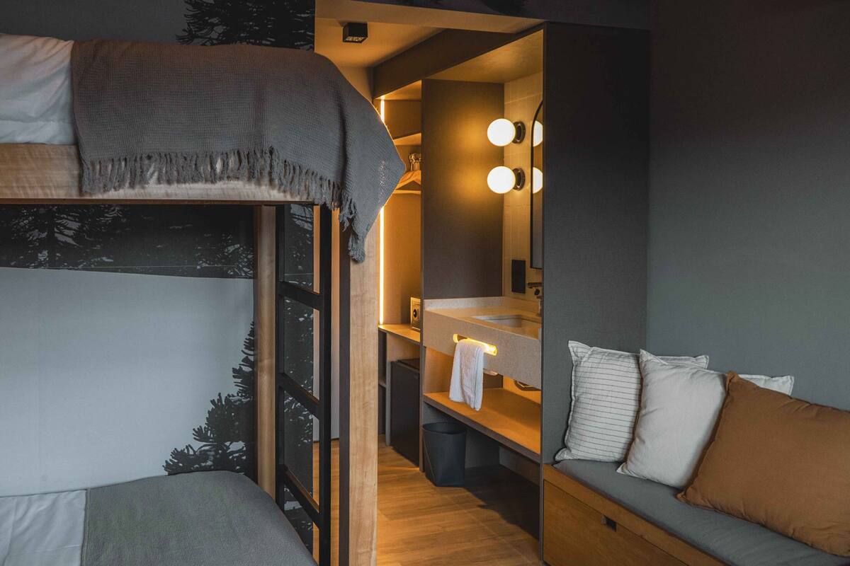 A compact bedroom with a bunk bed, a small vanity with a mirror and lights, and a sofa with pillows.