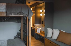 Een kleine slaapkamer met een stapelbed, een klein kaptafeltje met spiegel en verlichting, en een slaapbank met kussens.