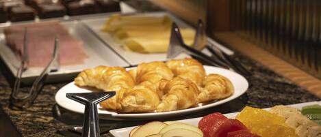 A buffet with various food items including pastries, fruits, and desserts.
