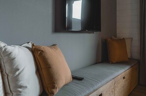Una habitación con un sofá azul claro, dos almohadas, un control remoto y un televisor montado en la pared.