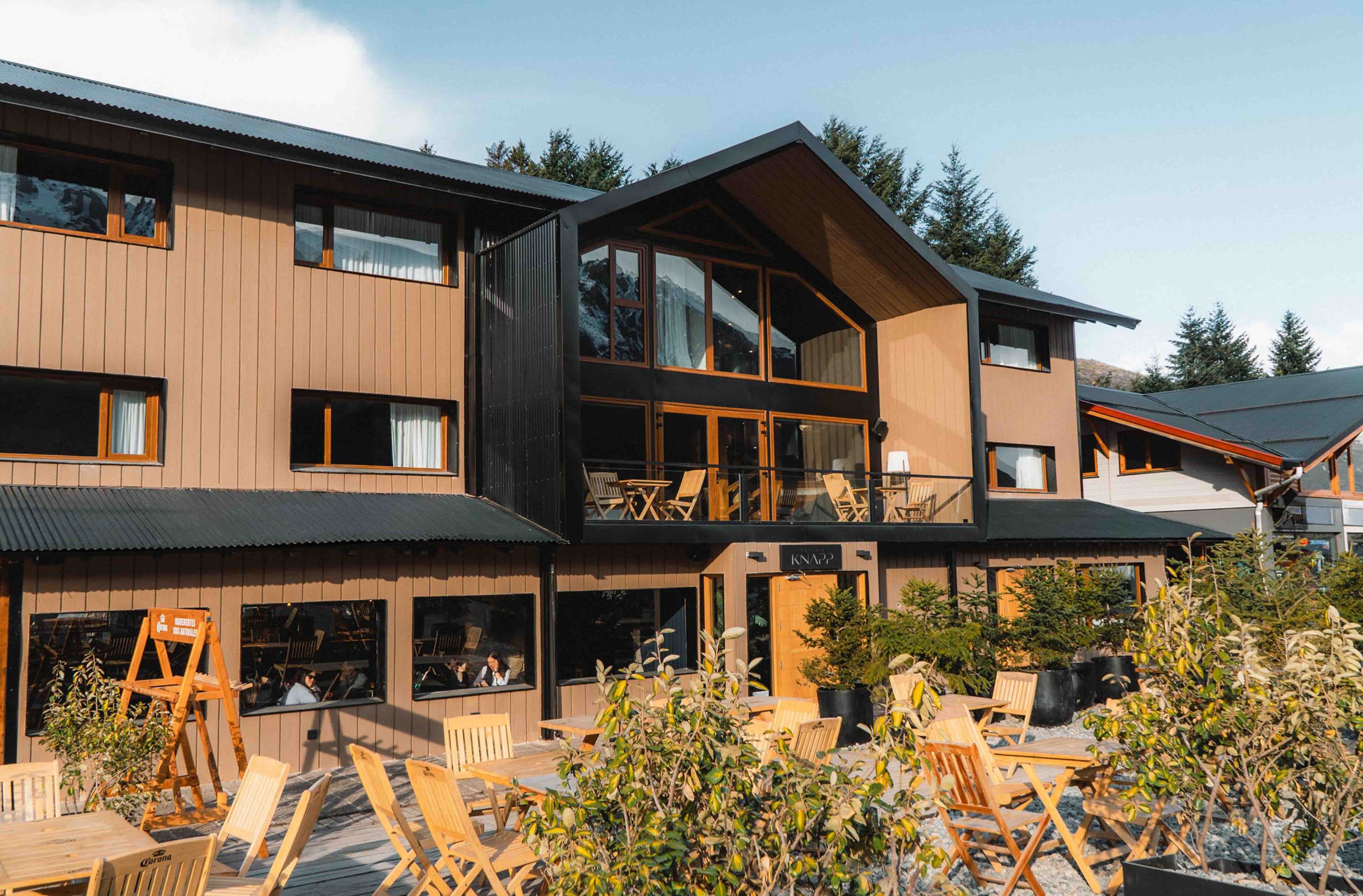 A modern two-story building with a wooden facade, large windows, and outdoor seating area.