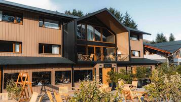 A modern two-story building with a wooden facade, large windows, and outdoor seating area.
