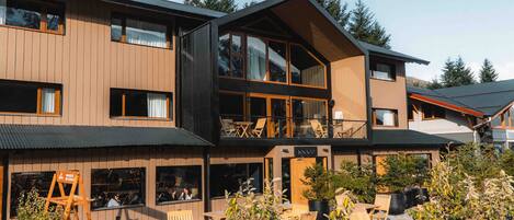 A modern two-story building with a wooden facade, large windows, and outdoor seating area.