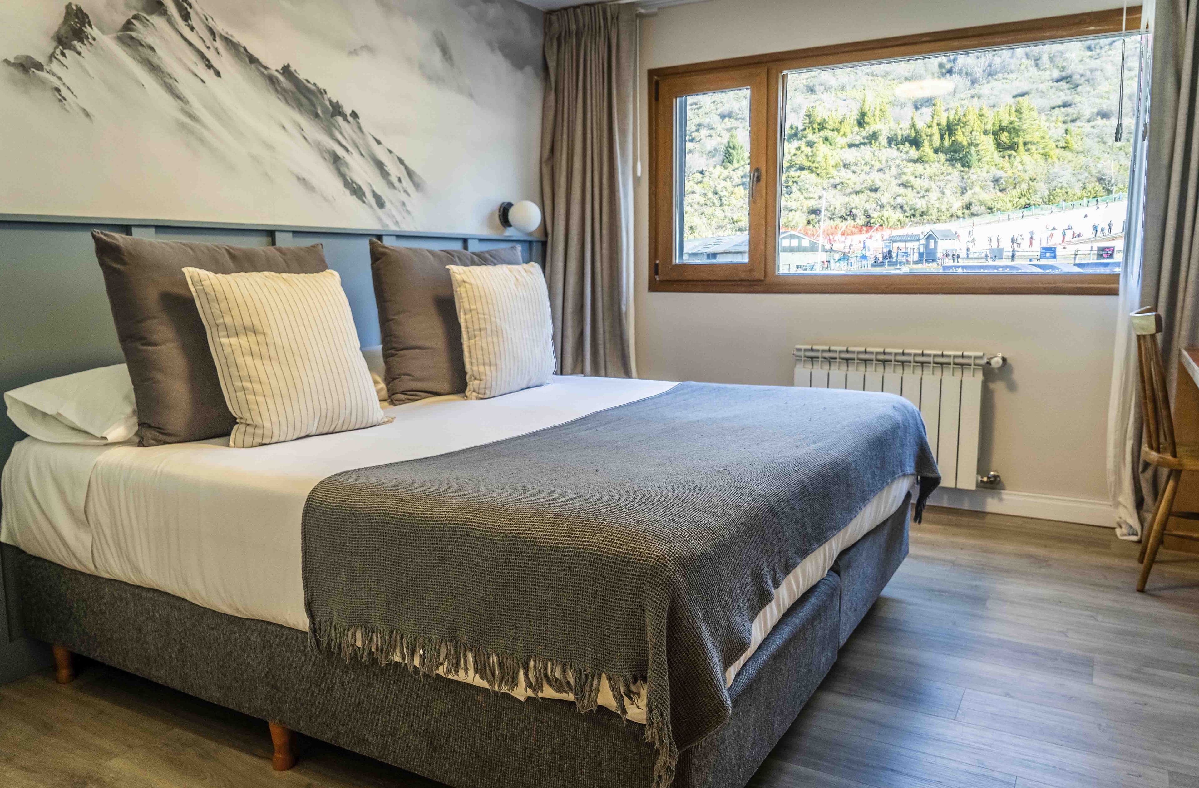 Een bed met een grijs-wit dekbed, een grijze deken en gestreepte kussens.