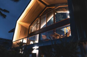 Un edificio moderno con grandes ventanales y fachada de madera al anochecer.