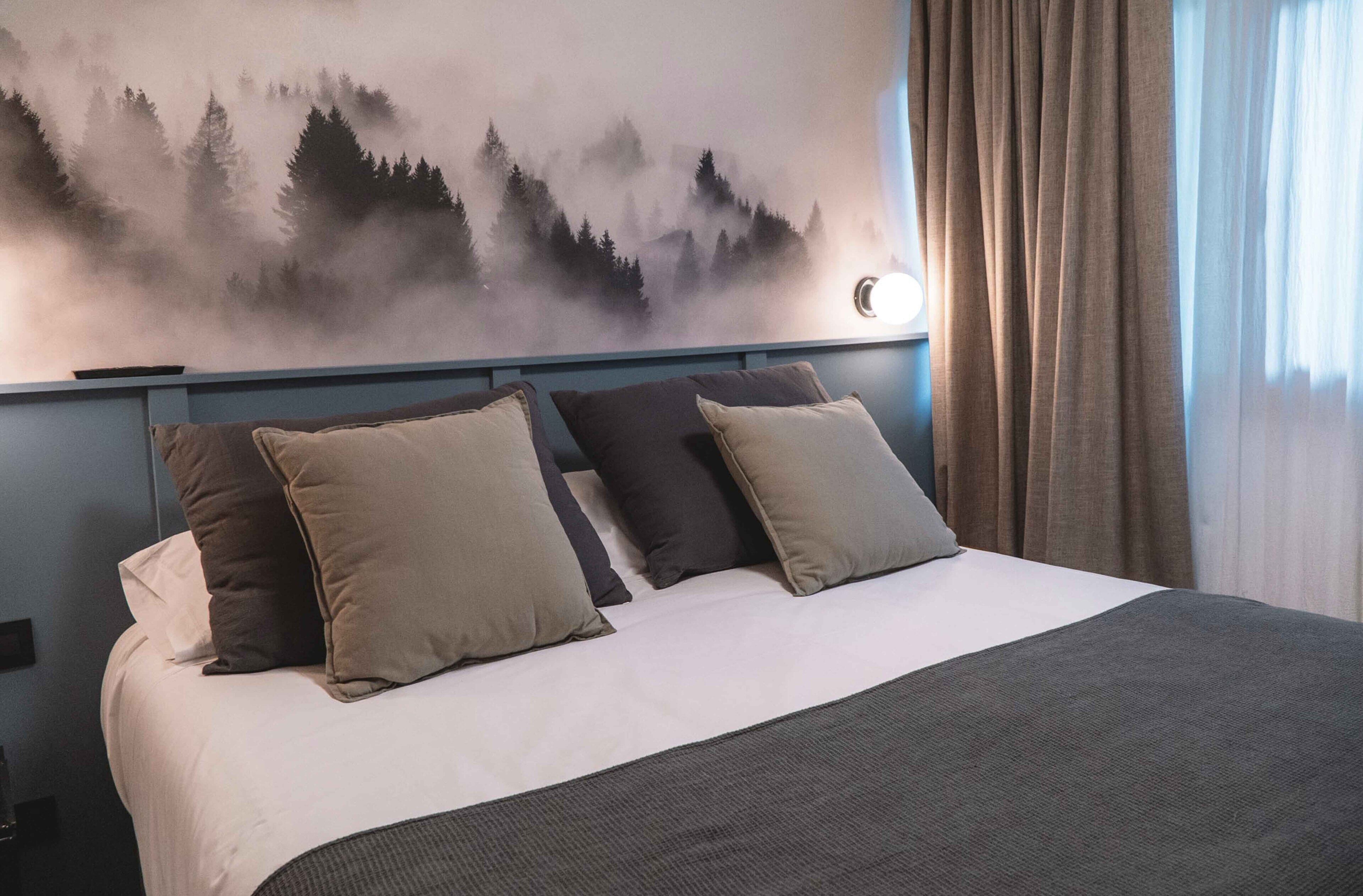 A neatly made bed with a white and gray bedspread, two beige and one dark gray pillow, and a gray throw blanket.