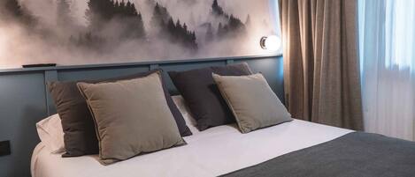 A neatly made bed with a white and gray bedspread, two beige and one dark gray pillow, and a gray throw blanket.