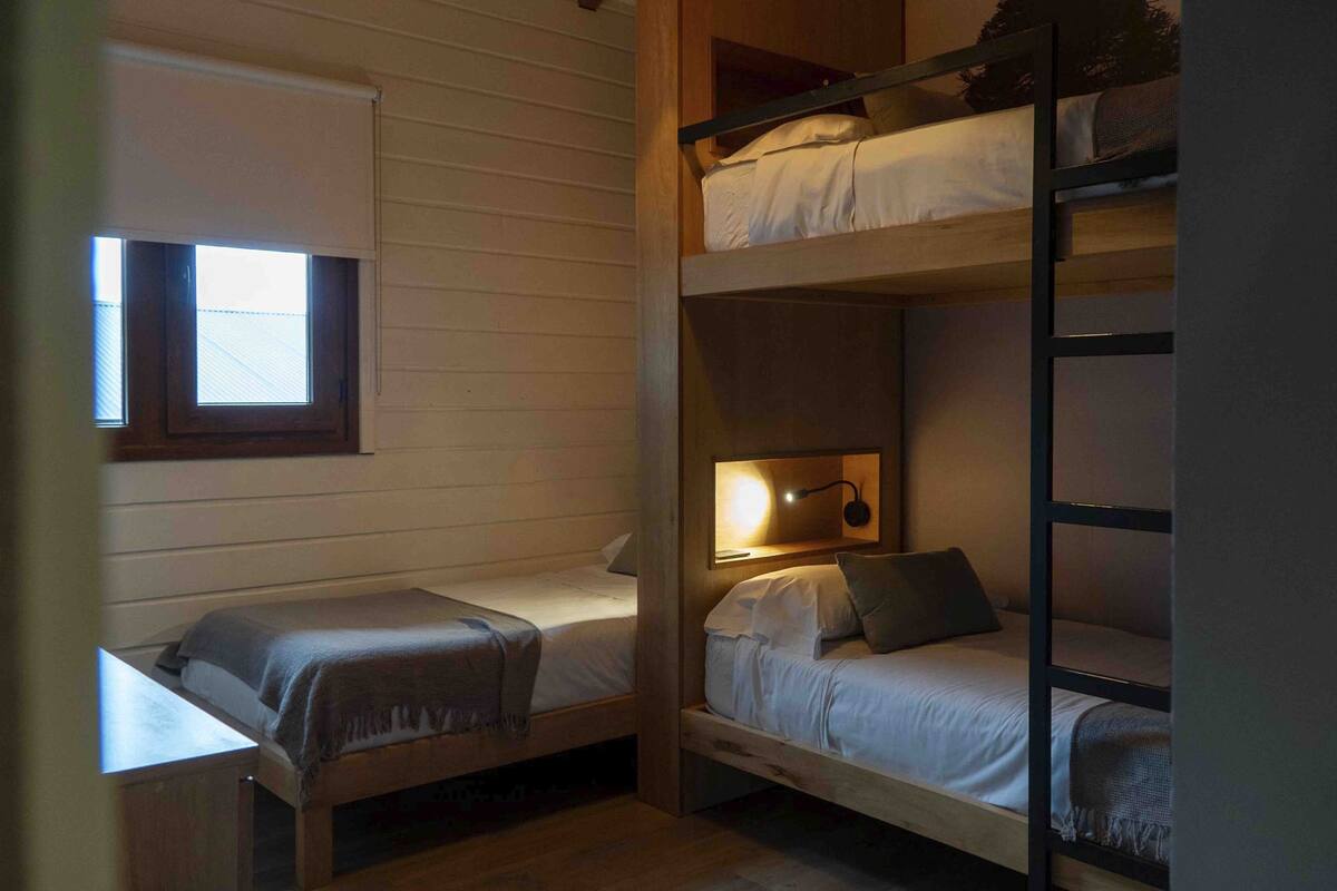 A dormitory room with bunk beds, a small window, and a wall-mounted lamp.