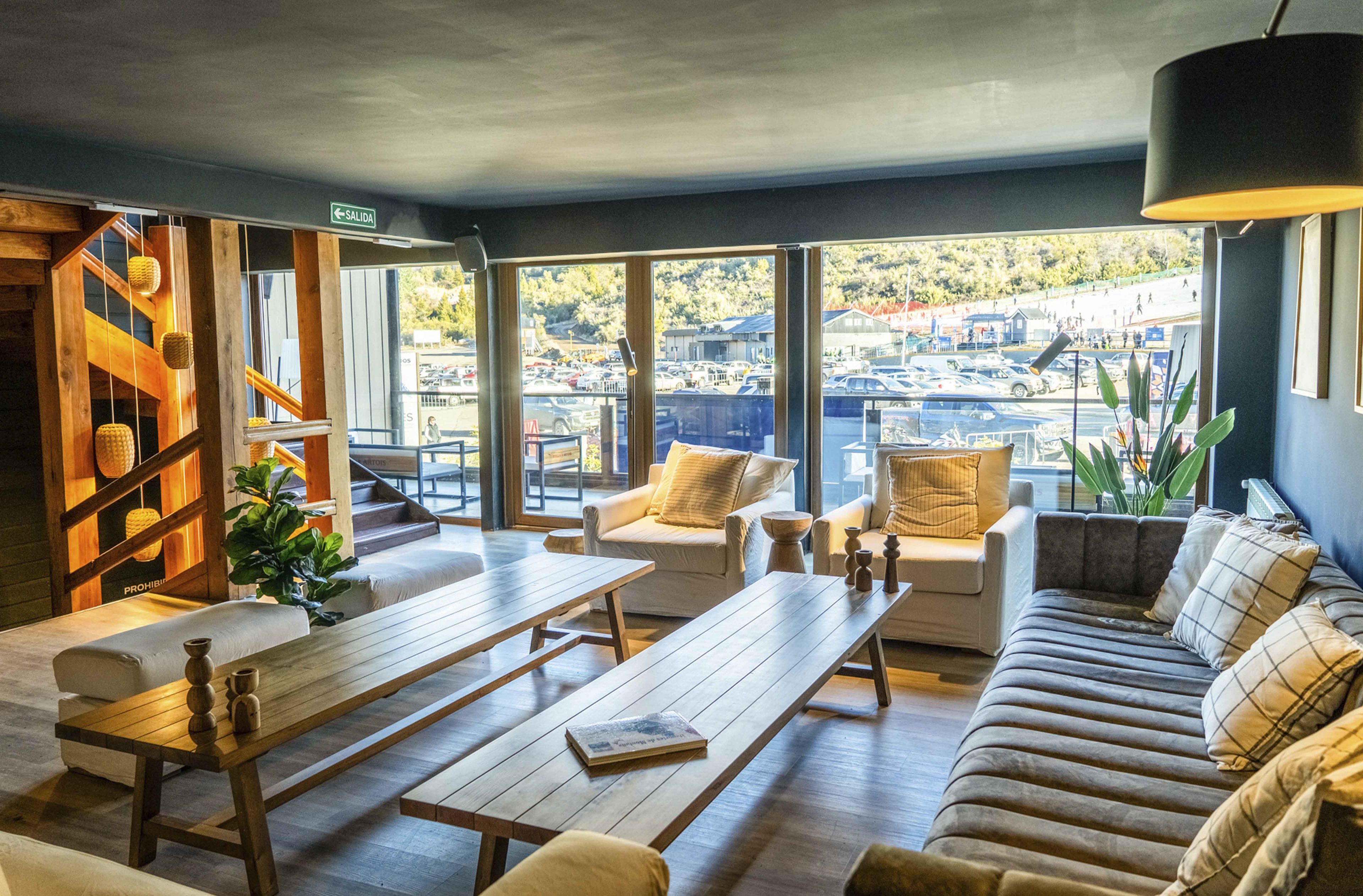 A modern interior with a wooden bench, sofa, and chairs, large windows with a view of a parking lot and buildings.