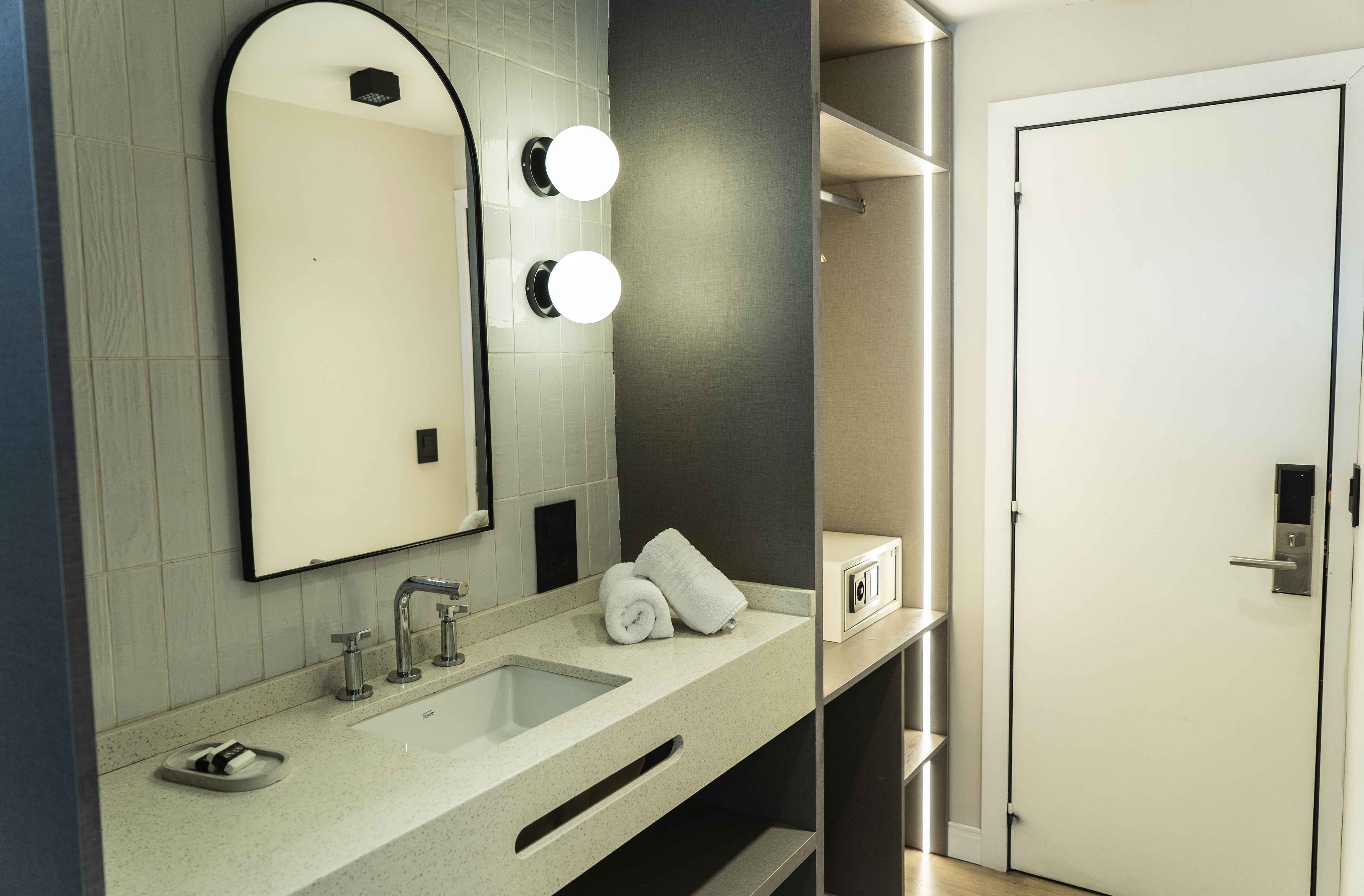 A modern bathroom with a large mirror, two round lights, a sink, and a towel rack.