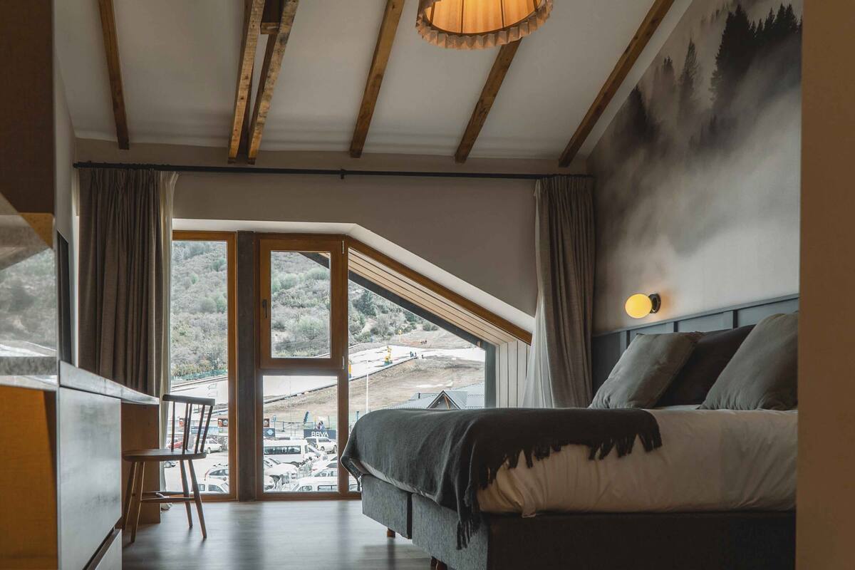 A bedroom with a bed, a chair, a large window, and a view of a snowy landscape.