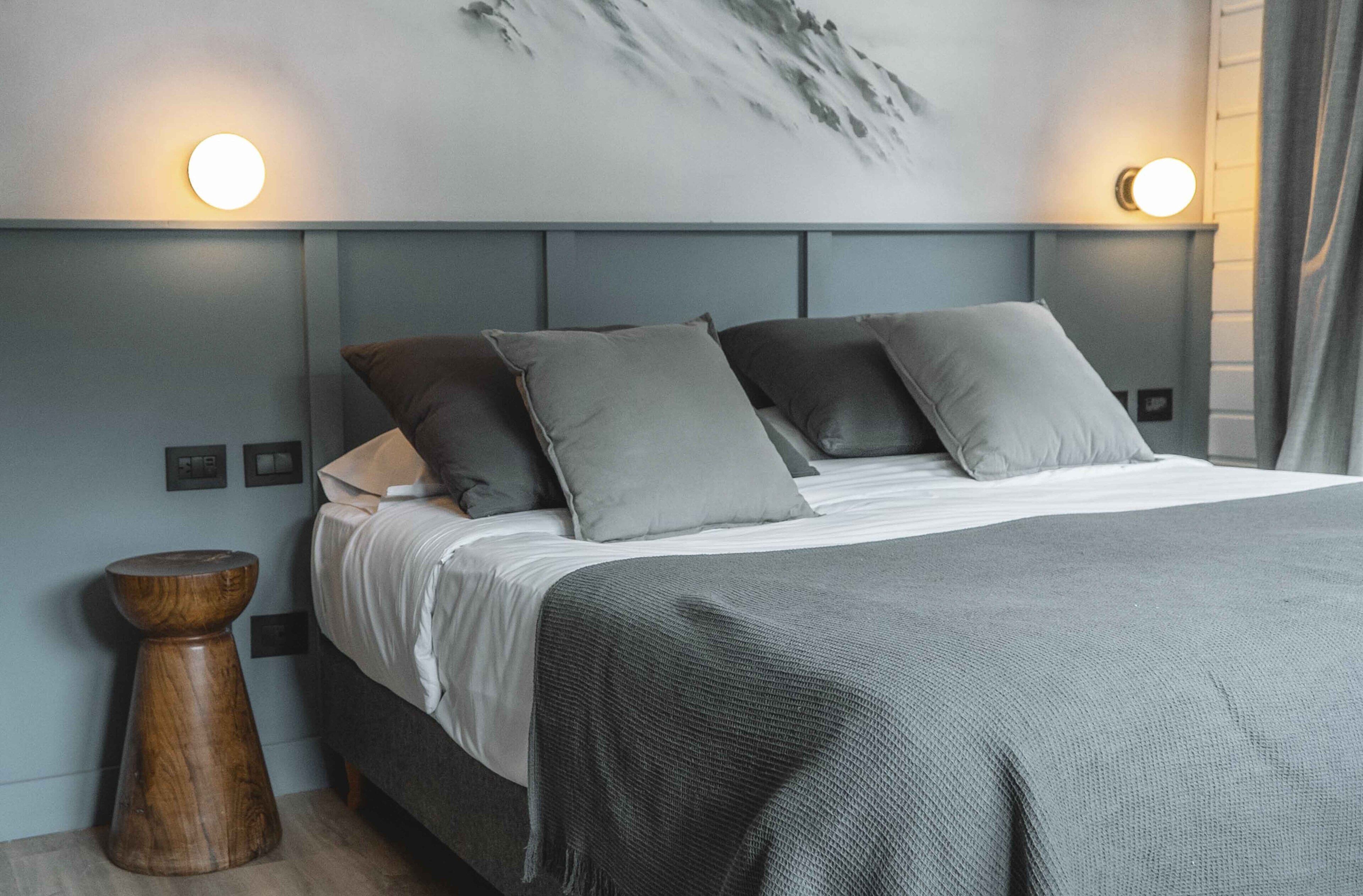 Une chambre moderne avec un lit, une literie grise et deux lampes fixées au mur.