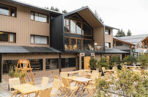 A modern building with a wooden facade, outdoor seating area with wooden tables and chairs, and a sign indicating a restaurant. - Refugio Knapp (San Carlos de Bariloche)