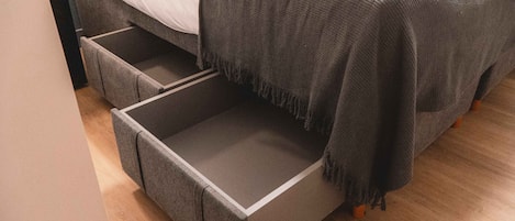 A bed with a grey blanket and a grey storage drawer beneath it.