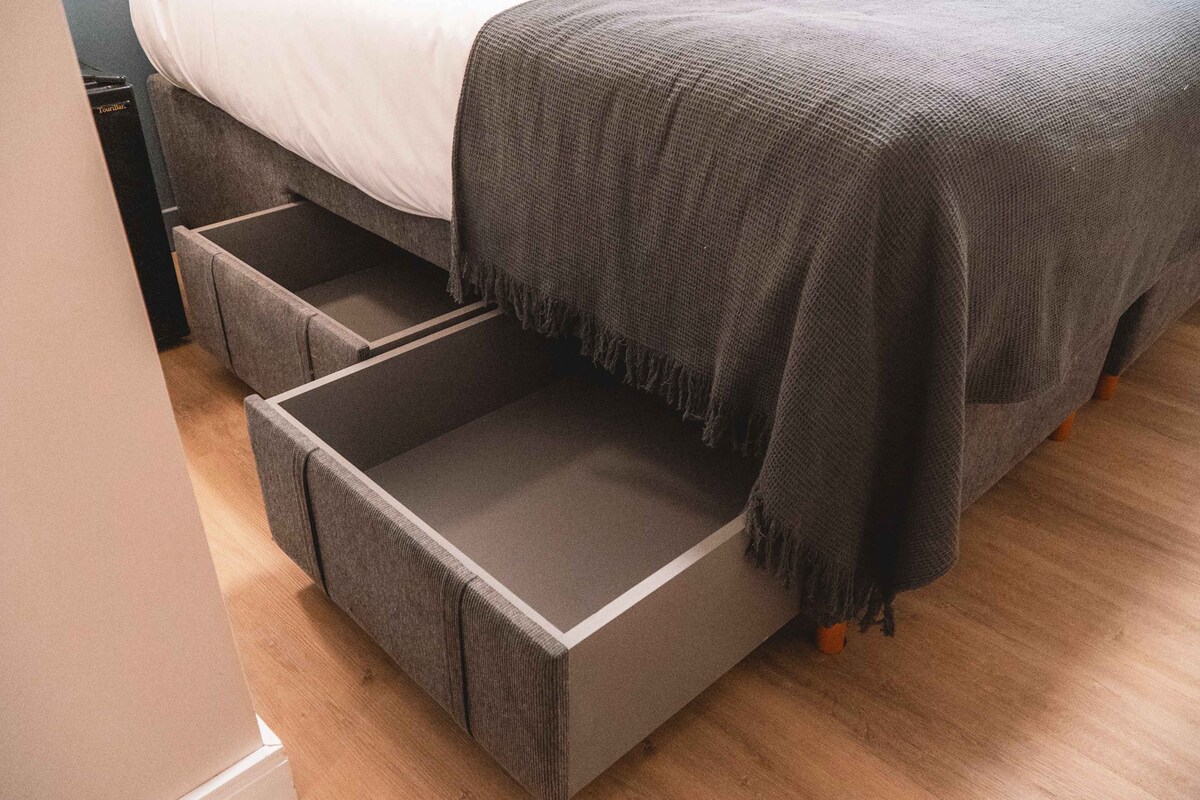A bed with a grey blanket and a grey storage drawer beneath it.