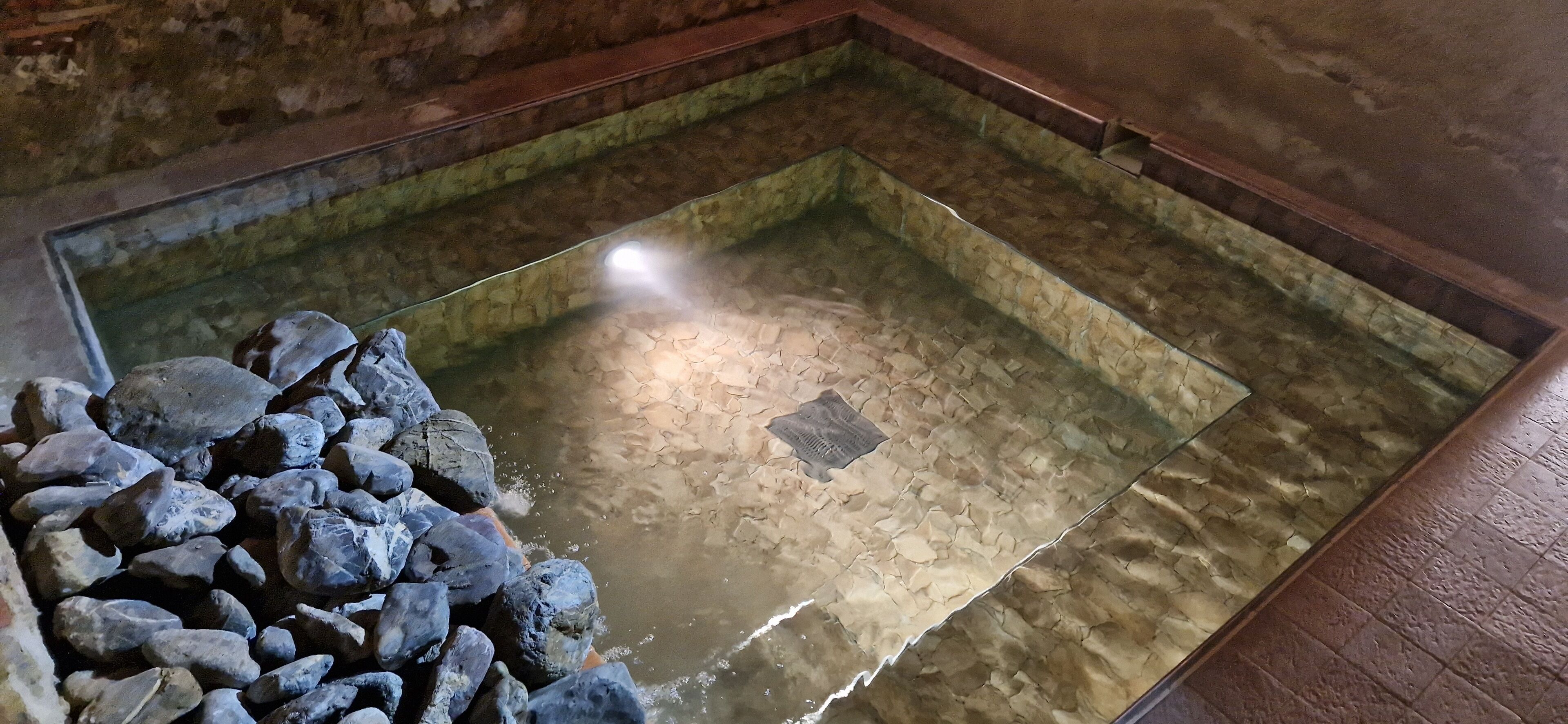 Une piscine bordée de pierres, avec une eau claire et un sol carrelé.