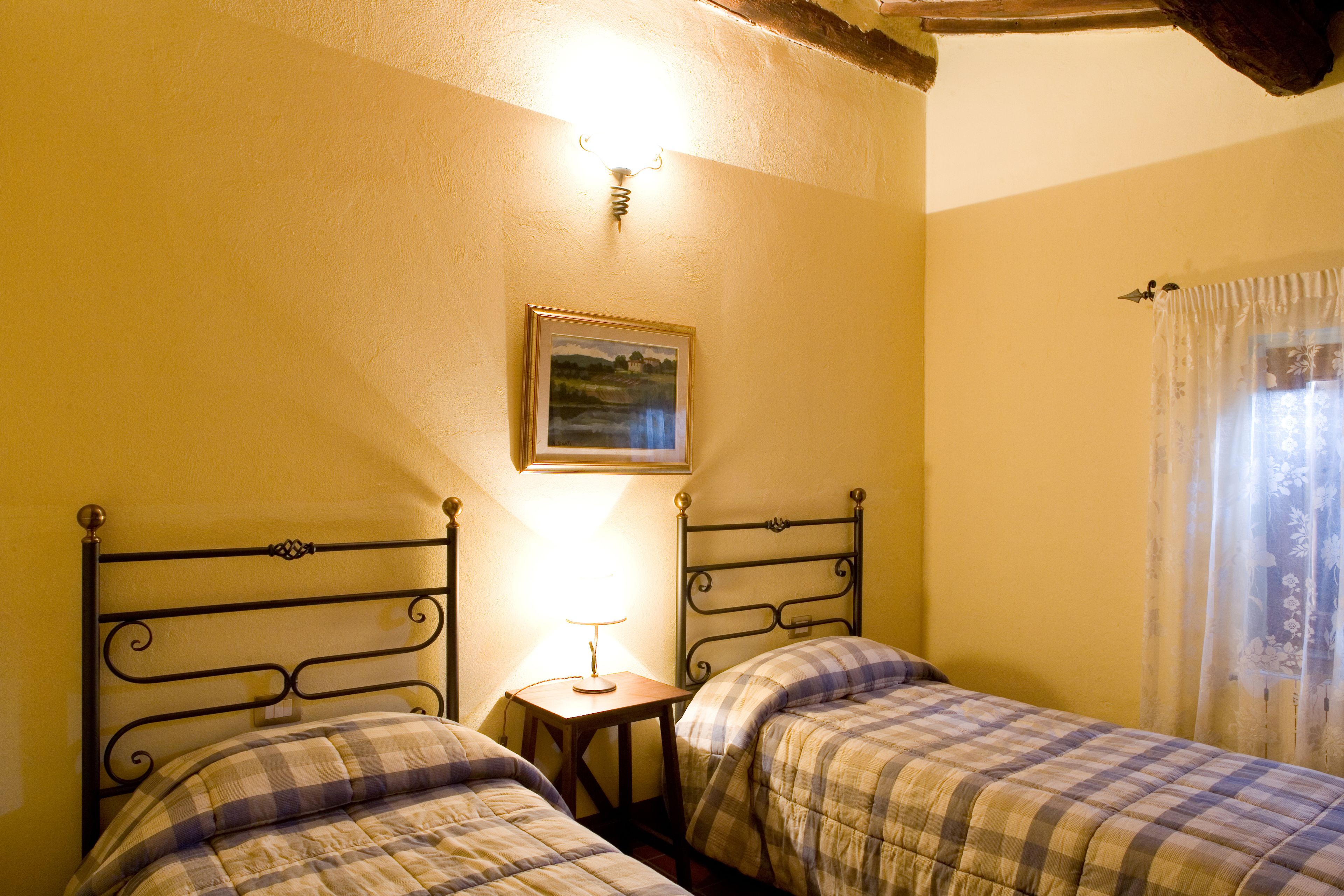 A bedroom with two beds, a small bedside table, a lamp, and a painting on the wall.