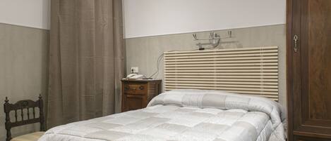 A bedroom with a bed, a nightstand, a wooden chair, and a wardrobe.