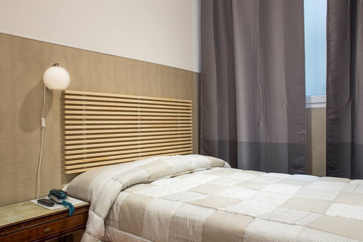 A bedroom with a wooden headboard, a bedside table with a lamp, and a bed with a quilt.