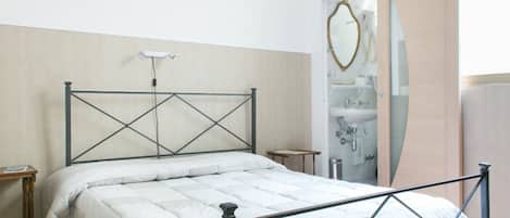 Ein Schlafzimmer mit einem Bett, einem Nachttisch, einem Spiegel und einem Badezimmer mit Waschbecken und Handtuchhalter.