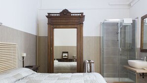 A bedroom with a large bed, a wooden wardrobe, a glass shower enclosure, and a bathroom with a sink and mirror. - Loggia Fiorentina (Florence)