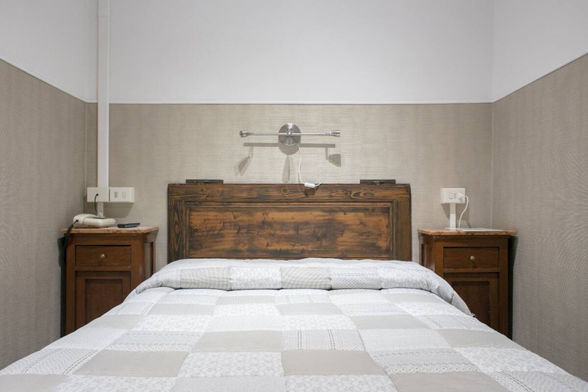 A bedroom with a wooden headboard, a quilted bedspread, two bedside tables with lamps, and a wall-mounted towel rack.