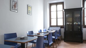 A classroom with blue chairs and tables, a black cabinet, and two framed pictures on the wall. - Loggia Fiorentina (Florence)