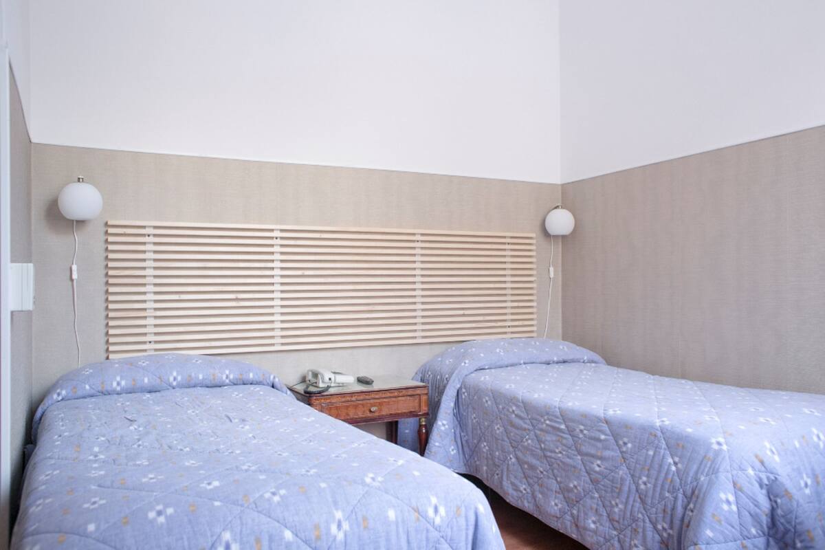 A bedroom with two beds, wooden blinds, a nightstand, and a lamp.