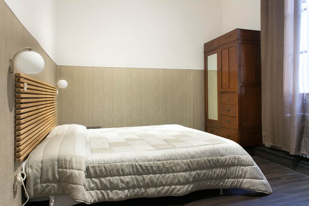 A bedroom with a bed, wooden headboard, a wardrobe, and a wall-mounted lamp.
