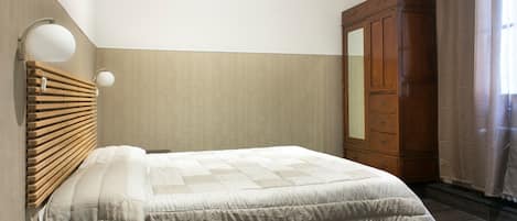 A bedroom with a bed, wooden headboard, a wardrobe, and a wall-mounted lamp.