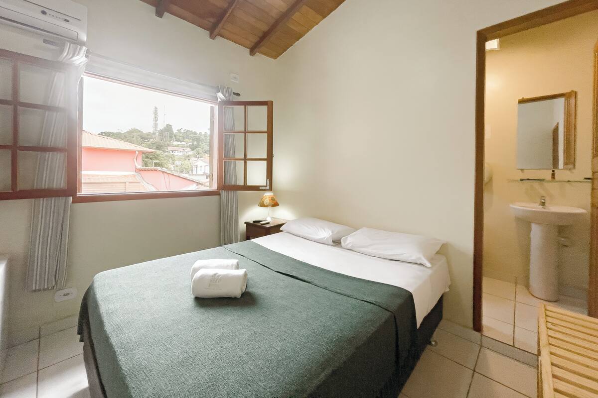 A bedroom with a bed, a window with curtains, a bedside lamp, and a view of the outside.