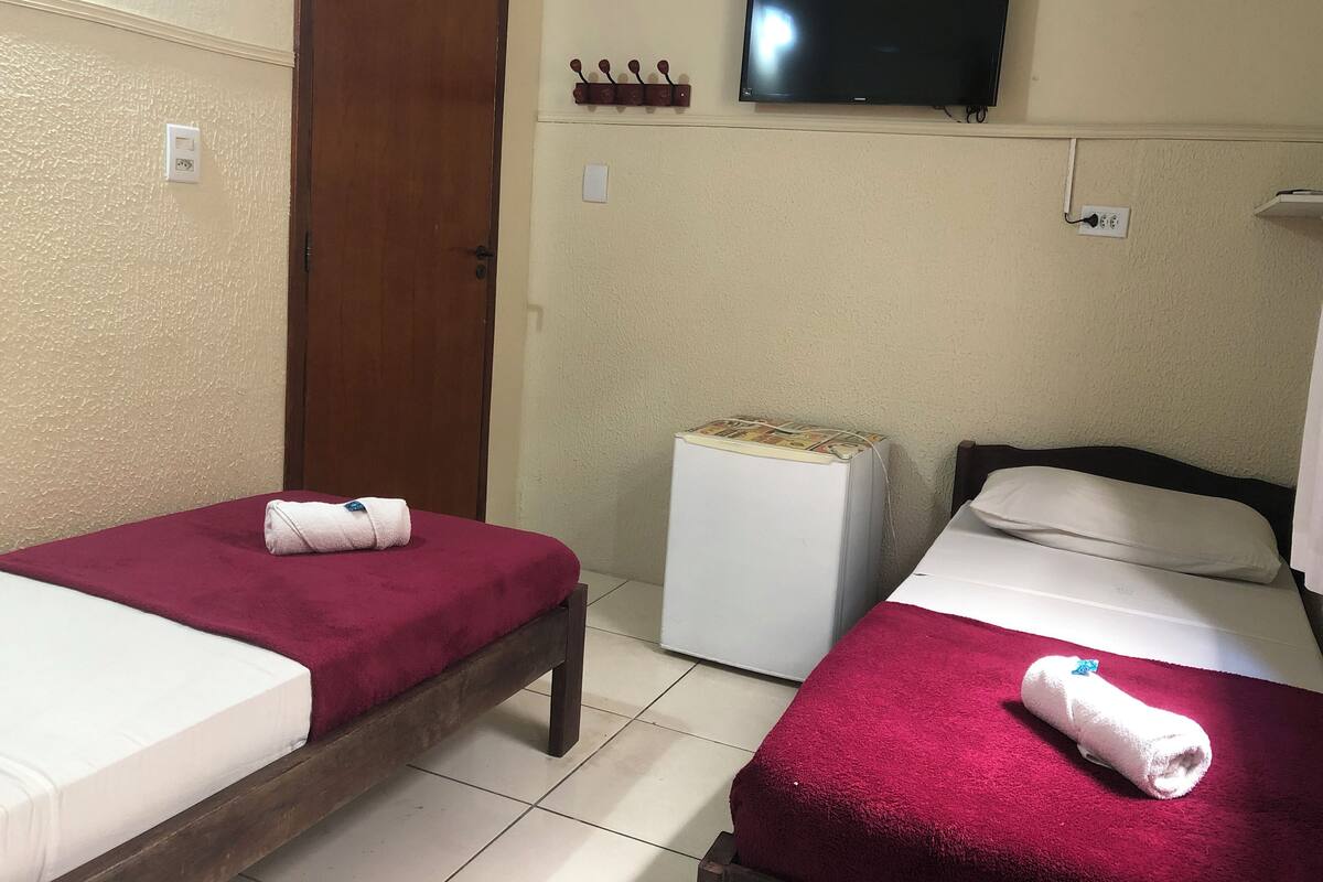 A hotel room with two beds, a television mounted on the wall, and a small white refrigerator.