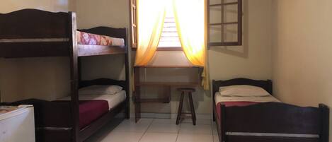 A dormitory room with bunk beds, a desk, a chair, and a TV.