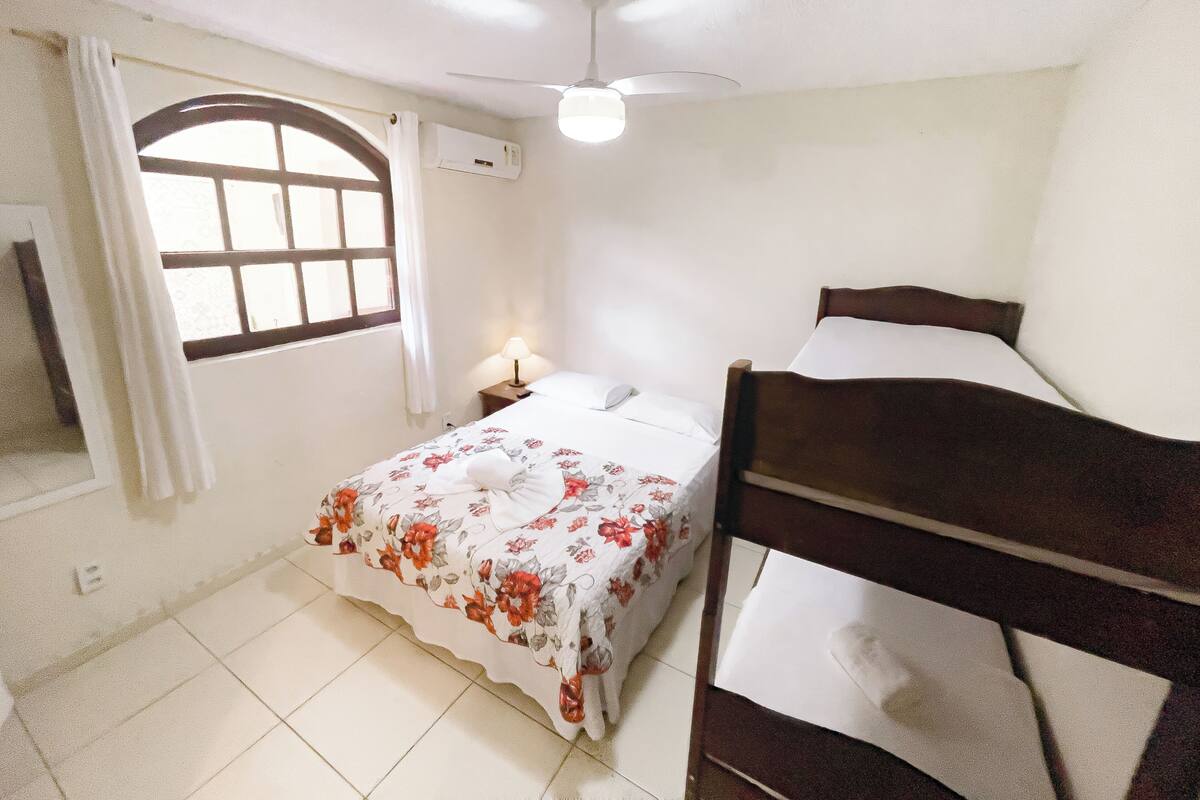 A bedroom with a bed, a window, a ceiling fan, and an air conditioning unit.