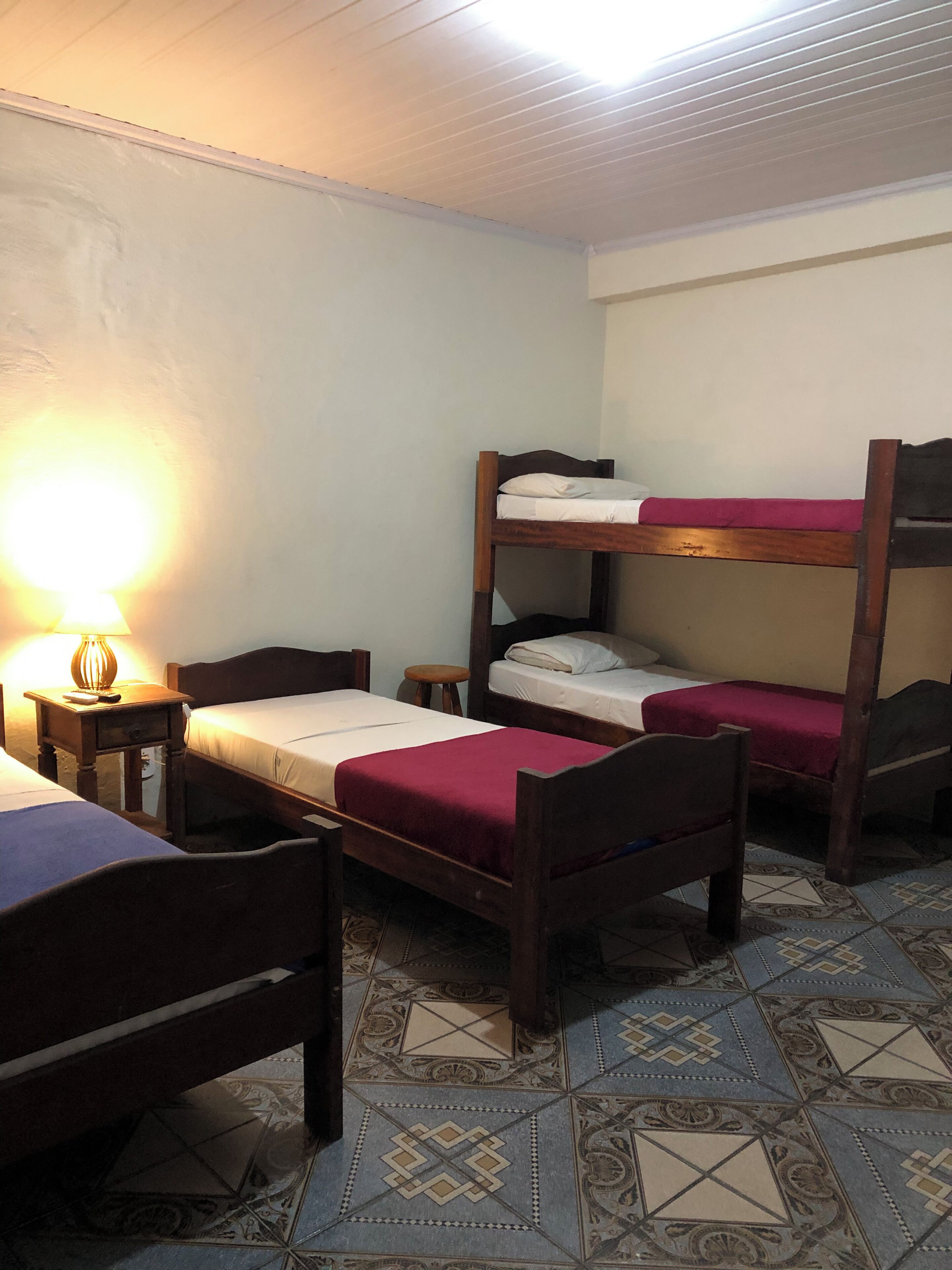 Une chambre de dortoir avec des lits superposés, une petite table, une lampe et des carreaux de sol à motifs.