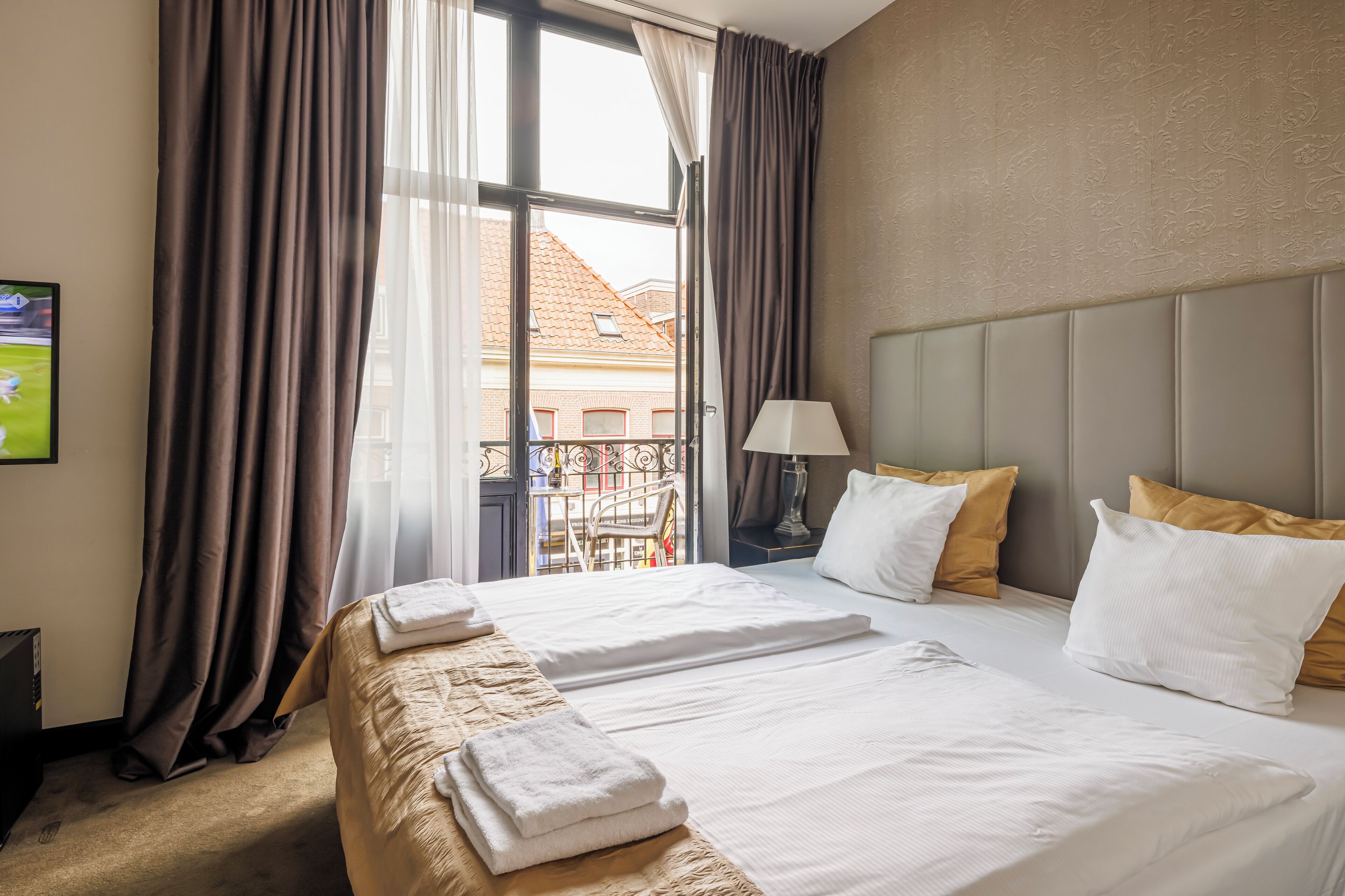 Habitación de hotel con dos camas, televisión, lámpara y vistas a edificios.