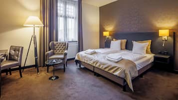 Camera d'albergo con un letto grande, due lampade sui comodini, una sedia, una lampada da terra e vista sull'esterno attraverso una finestra.