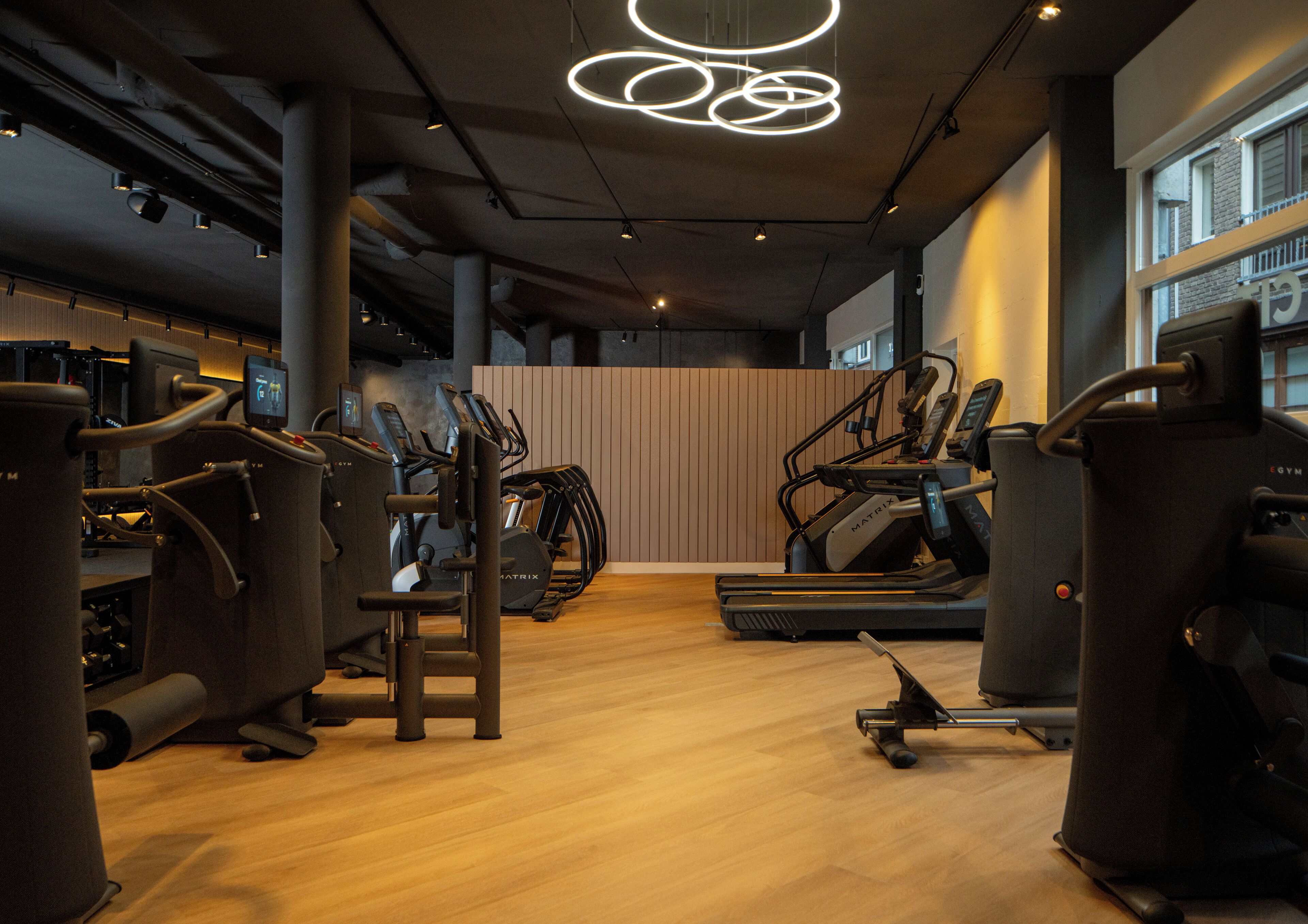 Un gimnasio moderno con máquinas de cardio, estaciones de pesas y piso de madera.