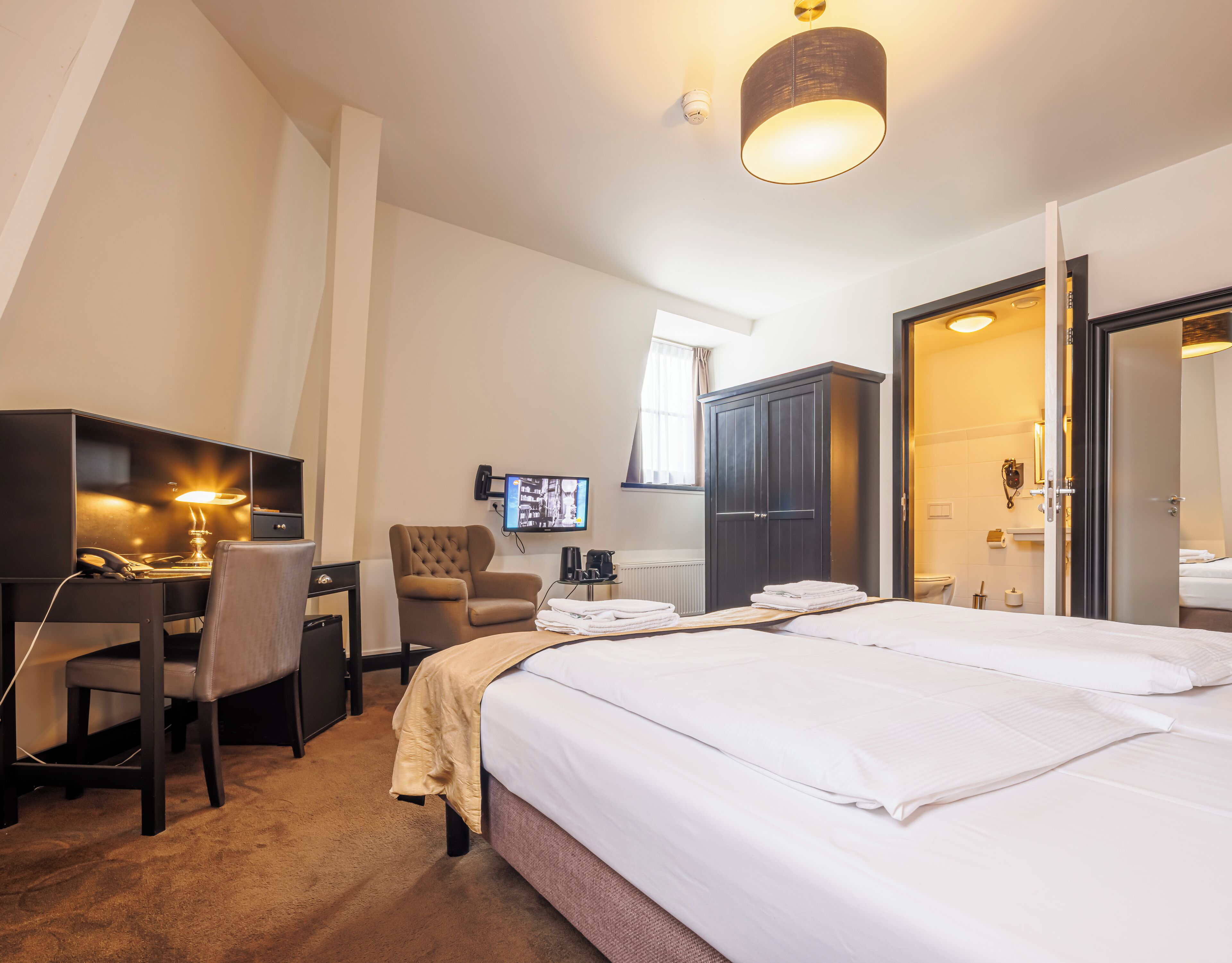 A hotel room with a bed, desk, chair, TV, wardrobe, and bathroom.