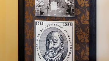 Fotografía histórica enmarco de una fábrica textil con trabajadores y maquinaria, y una moneda conmemorativa del 30 aniversario de Gelderland.